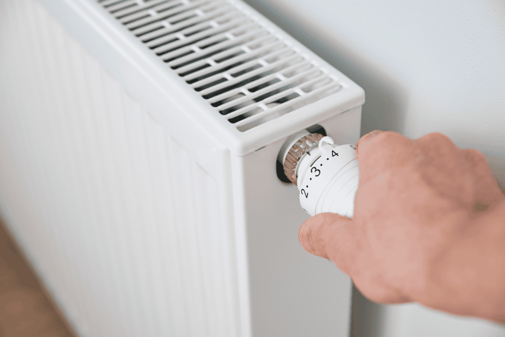 A hand adjusting the temperature dial on a white radiator, a setting that helps manage home comfort much like knowing how long a furnace lasts.