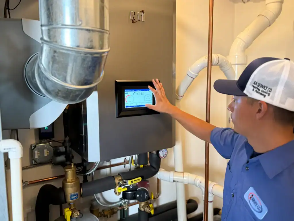 A technician in uniform operates a digital control panel on a wall-mounted boiler system surrounded by pipes and vents.
